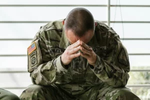 un homme en tenue de militaire aussi, penché en avant sa tête appuyée sur ses mains pointant